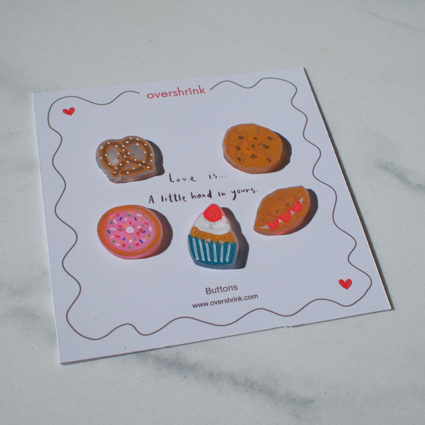 Card with illustrated buttons resembling donuts, cookies, and a cupcake on a marble surface.