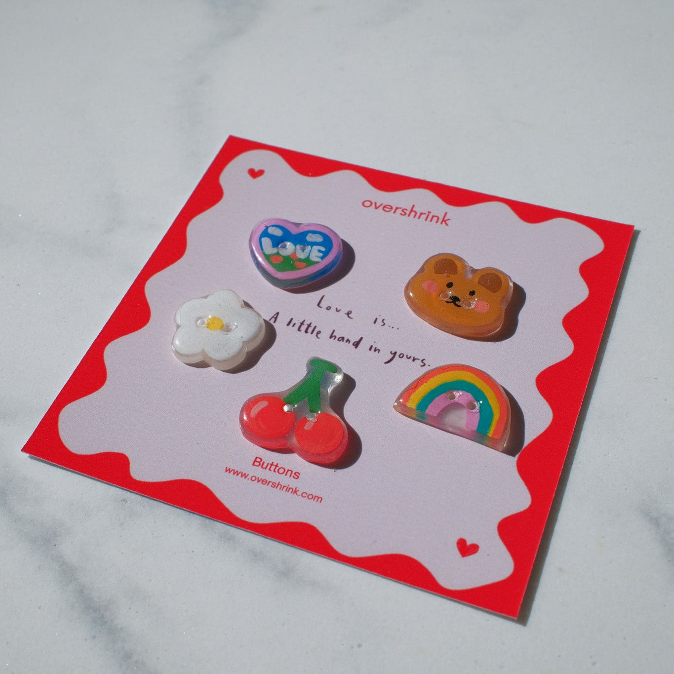 Set of colorful buttons on a red card with 'overshelink' branding, placed on a white surface.
