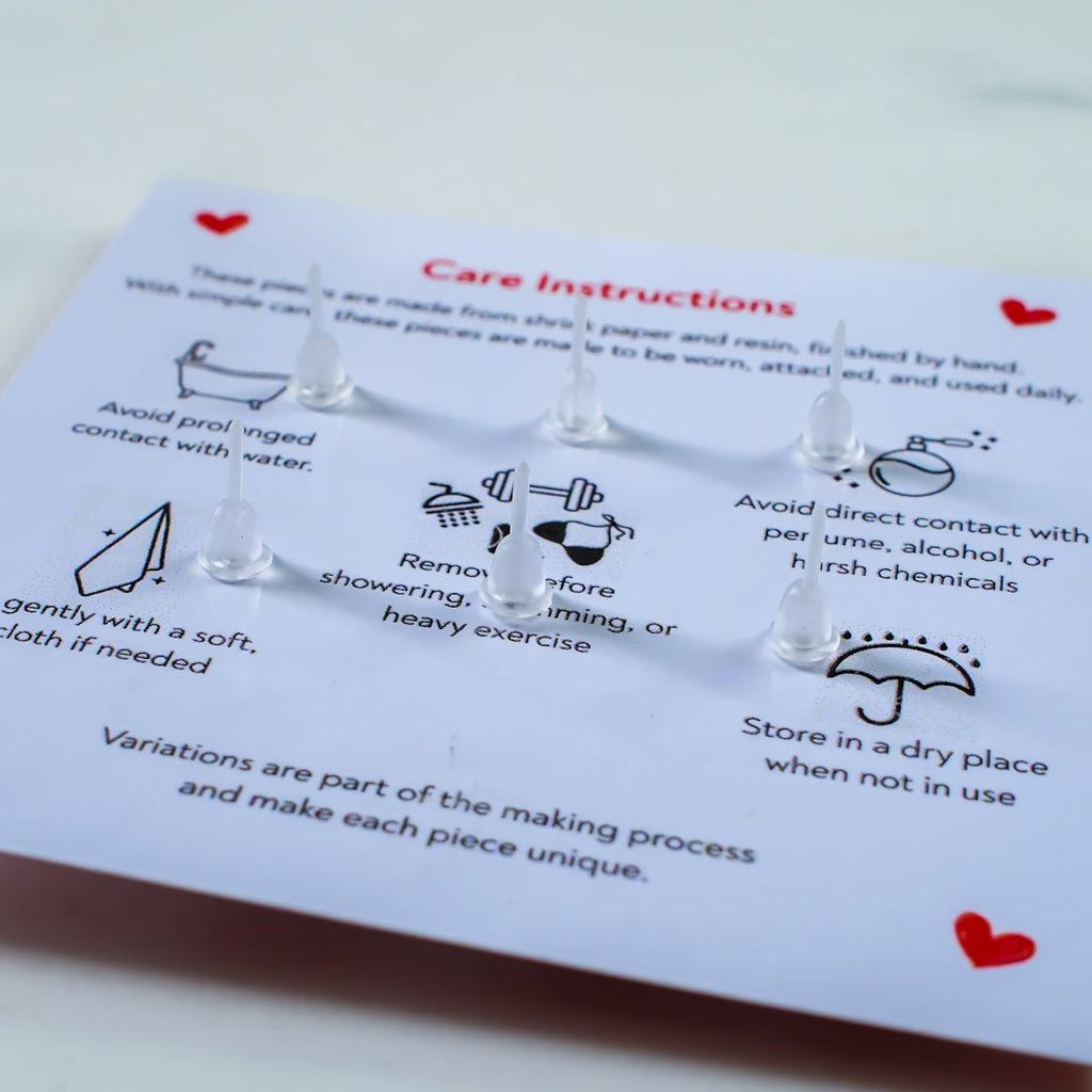 Pair of silver earrings on a card with care instructions on a light gray background