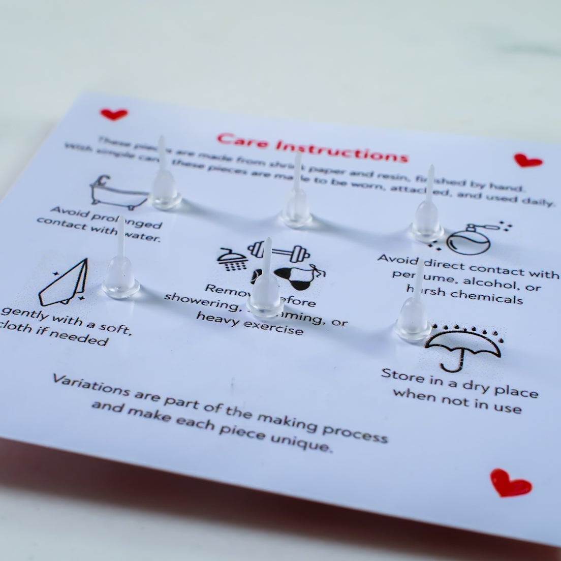 Pair of silver earrings on a card with care instructions on a light gray background