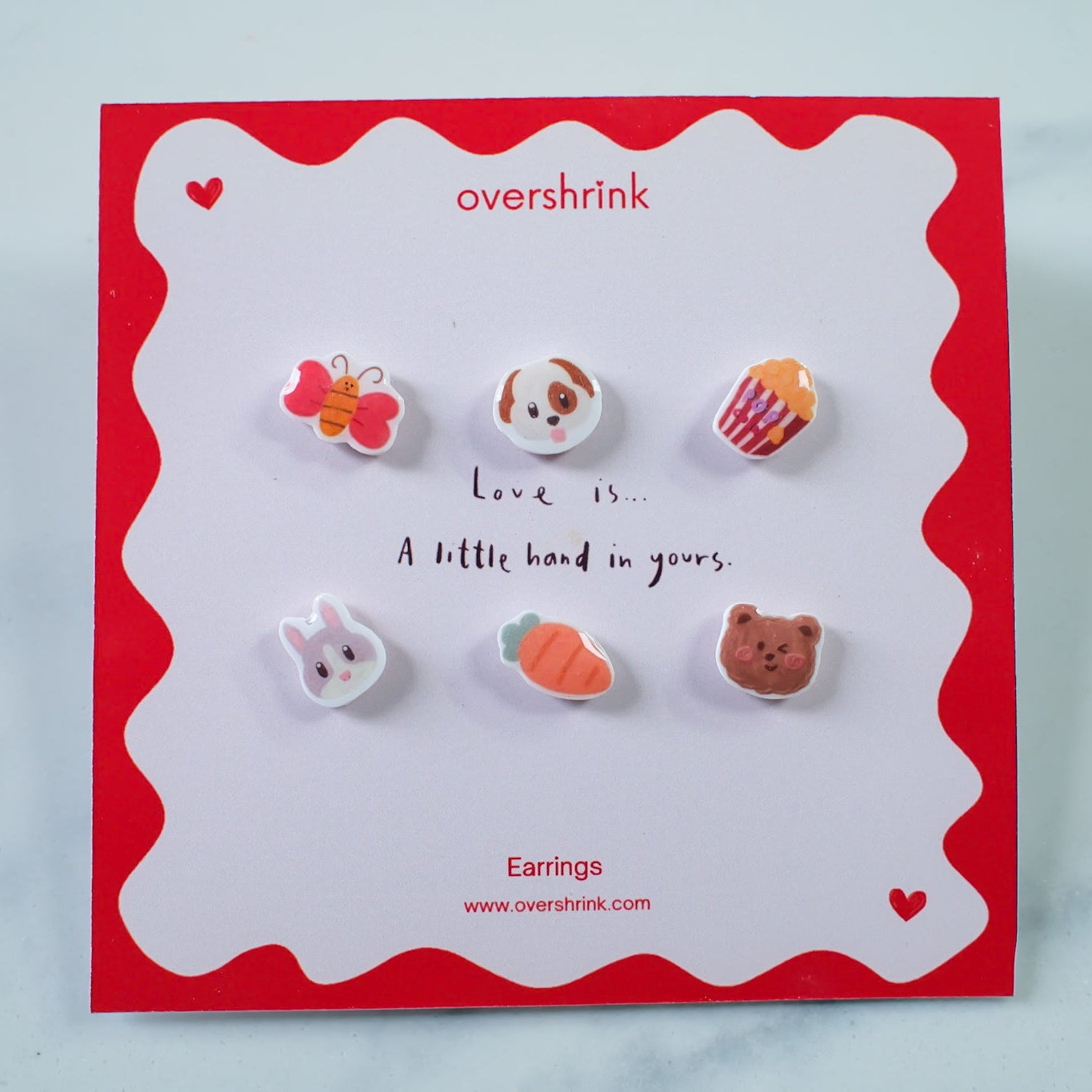 Set of small earrings on a 'overshrink' branded card with a red border.